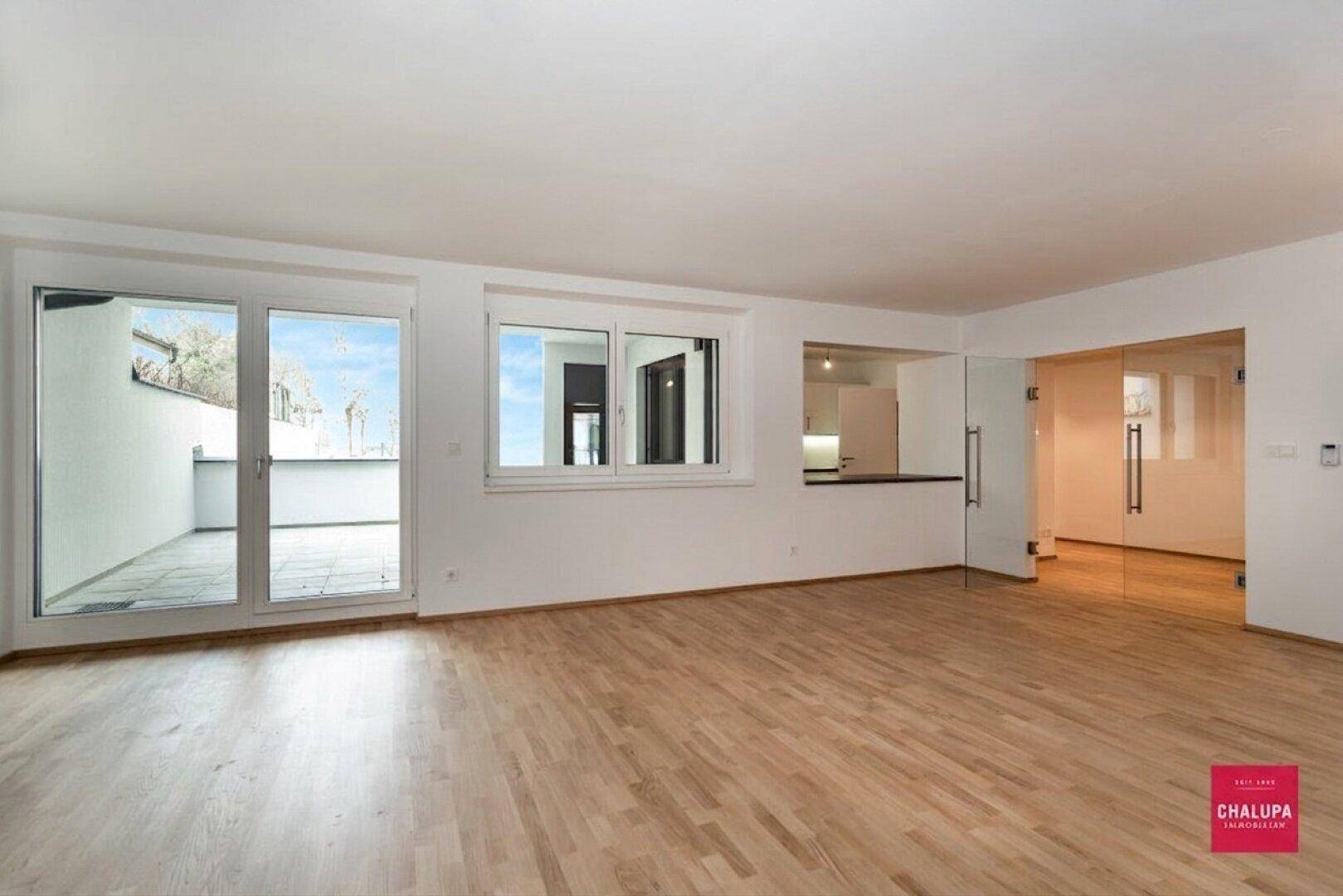 Helles Wohnzimmer mit Parkettboden, großen Glastüren zur Terrasse und Durchreiche zur Küche.