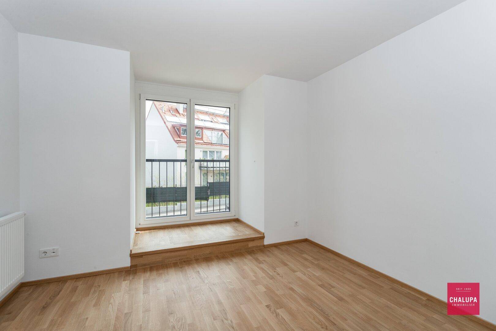 Freundliches Zimmer mit Parkettboden, weißen Wänden und einem französischen Balkon.
