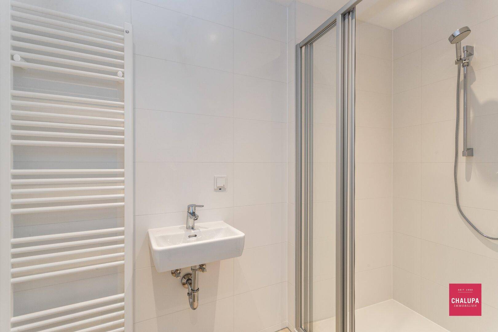 Helles Badezimmer mit Duschkabine, Waschbecken und beheiztem Handtuchhalter.