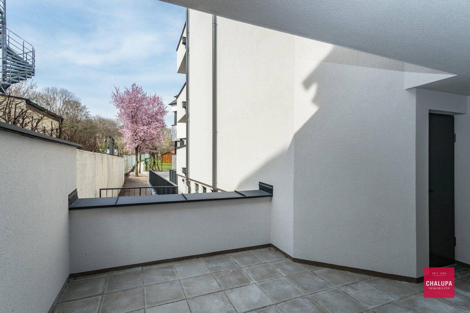 Geräumige Terrasse mit Fliesenboden und Blick auf die umliegenden Gebäude und Bäume.
