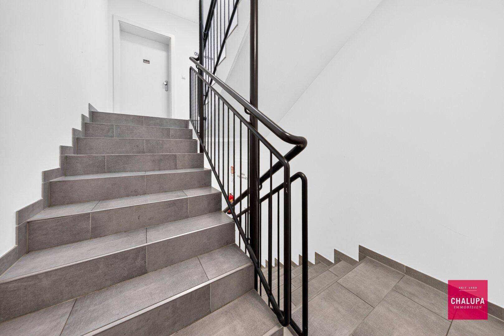 Modernes Treppenhaus mit grauen Fliesen und einem stabilen schwarzen Metallgeländer.