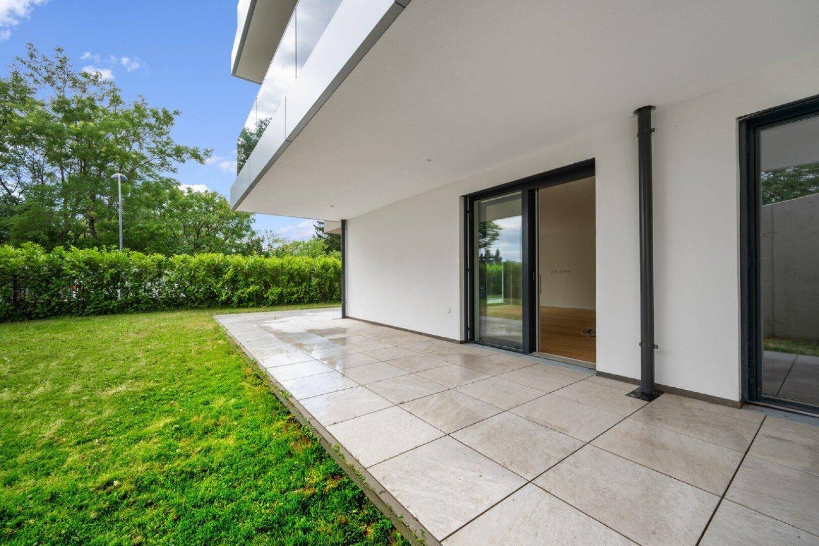 Helle Terrasse mit Zugang zum Garten und Blick ins Grüne, ideal für Entspannung im Freien.