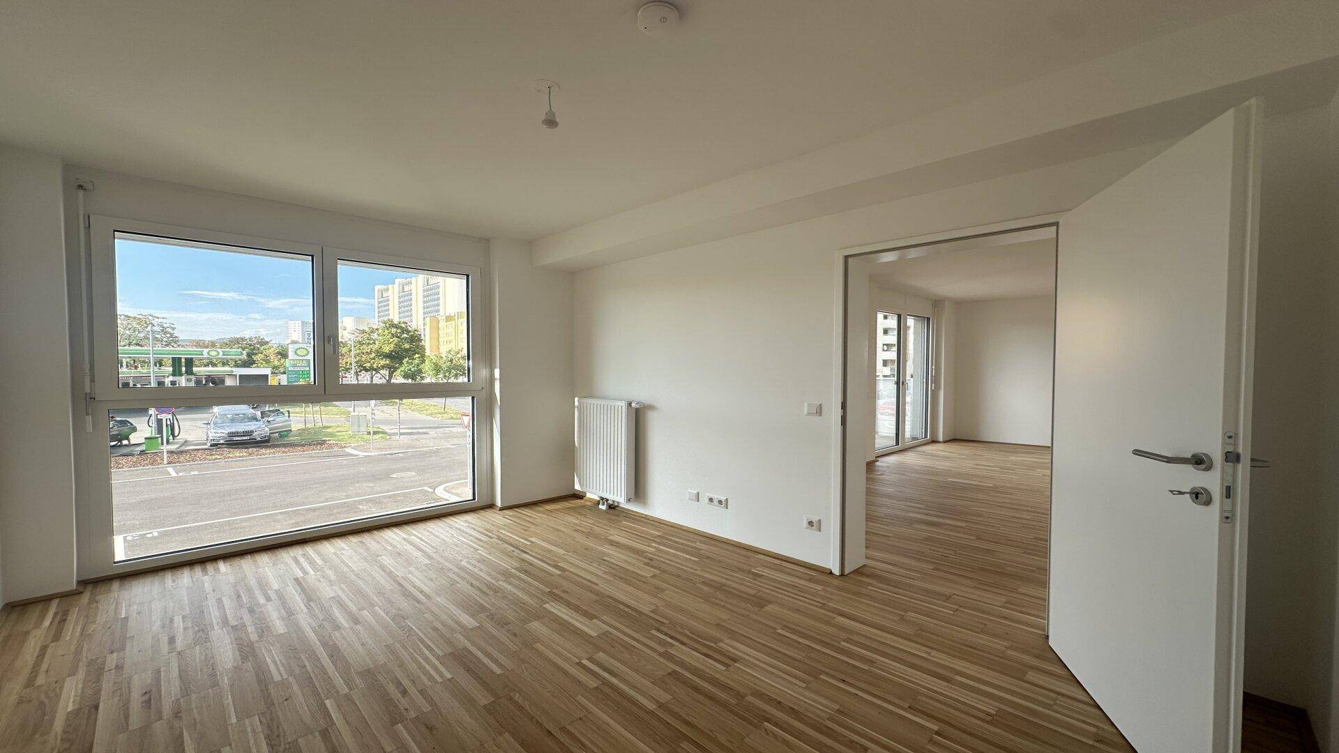 Helles Wohnzimmer mit Parkettboden und großen Fenstern, die einen Blick nach draußen bieten.