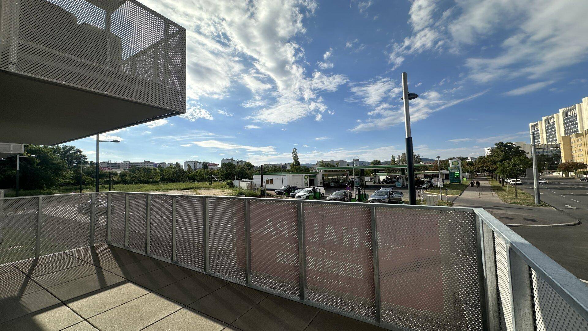 Balkon mit Blick auf die Stadt und eine Tankstelle, unter blauem Himmel.