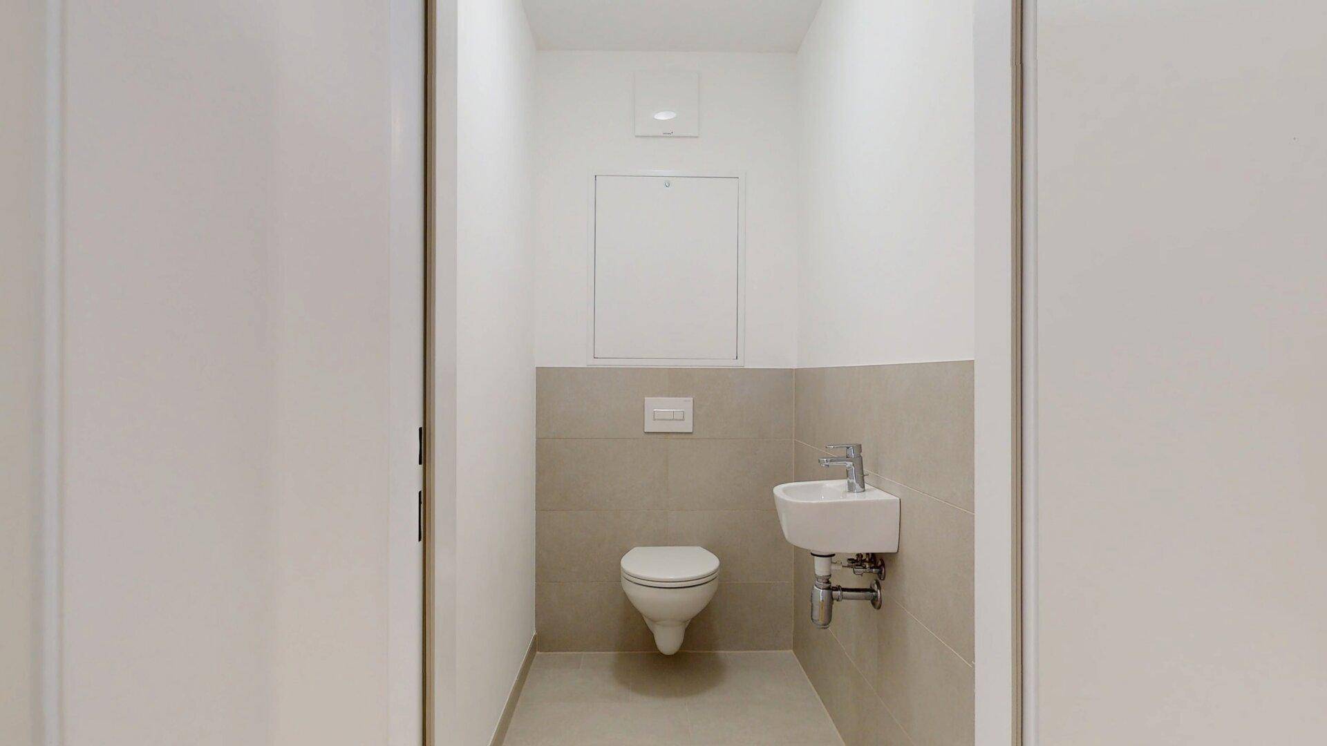 Separates WC mit Wandtoilette und kleinem Handwaschbecken, in neutralen Farben gehalten.