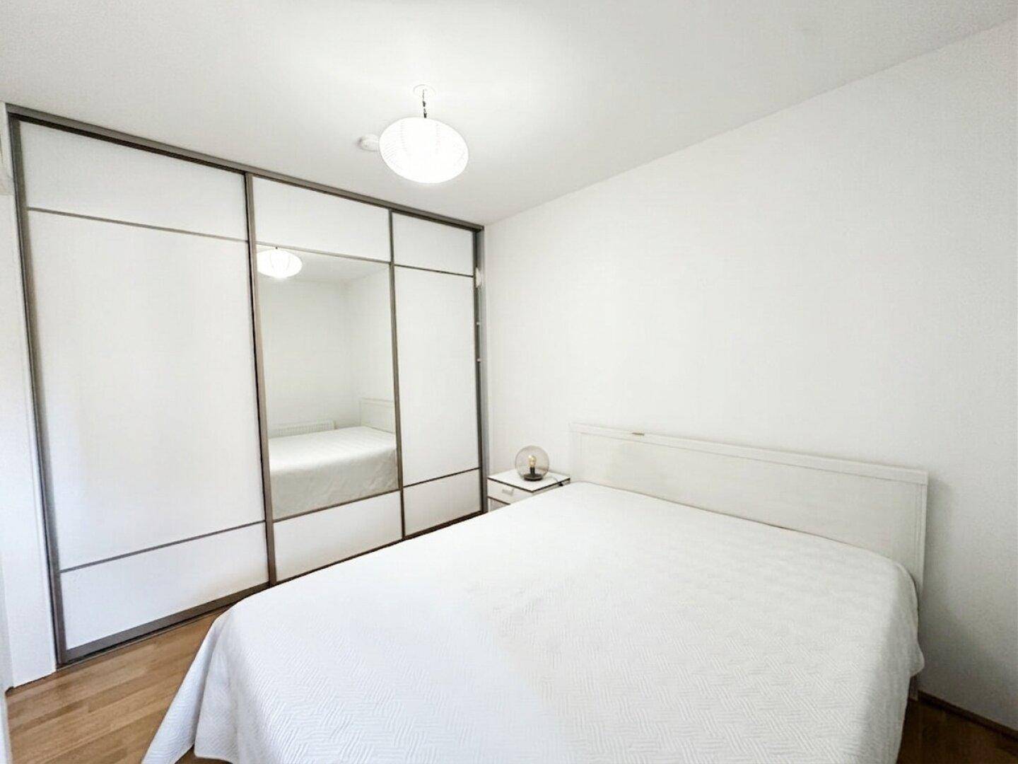 Schlafzimmer mit großem Einbauschrank, weißem Bett und Nachttisch, ideal für zusätzlichen Stauraum.