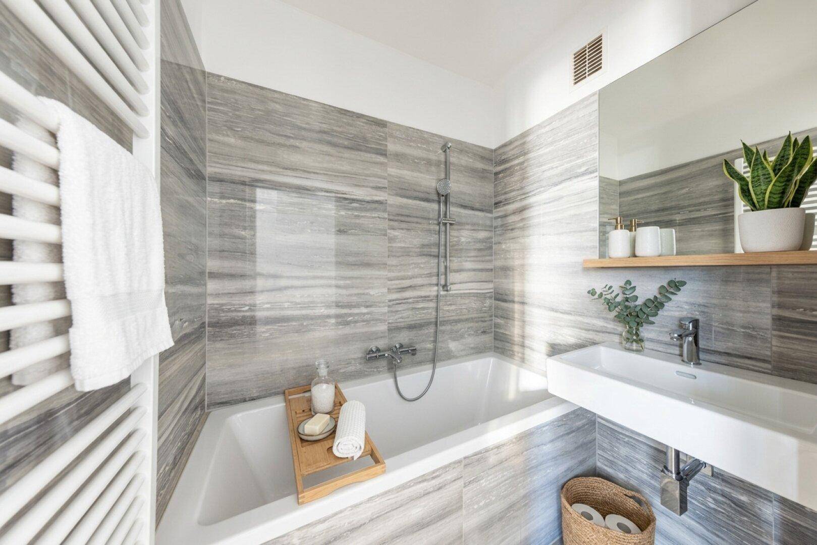 Modernes Badezimmer mit grauen Fliesen, Badewanne mit Duschfunktion und beheiztem Handtuchhalter.