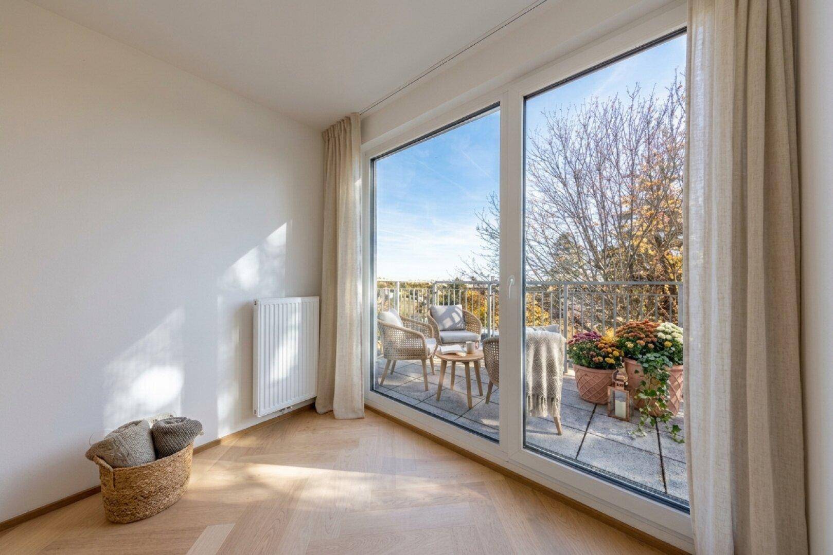 Heller Raum mit bodentiefen Fenstern, die Zugang zu einem möblierten Balkon bieten.