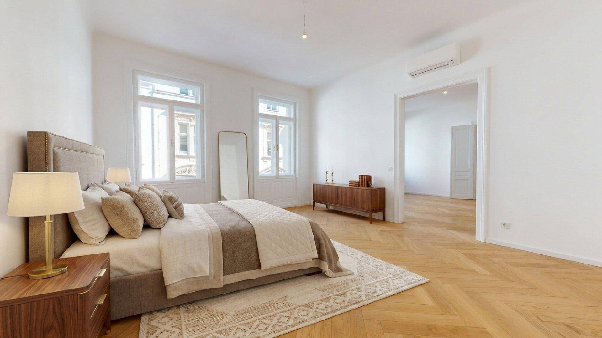 Geräumiges Schlafzimmer mit Doppelbett, Fischgrätparkett und großen Fenstern.