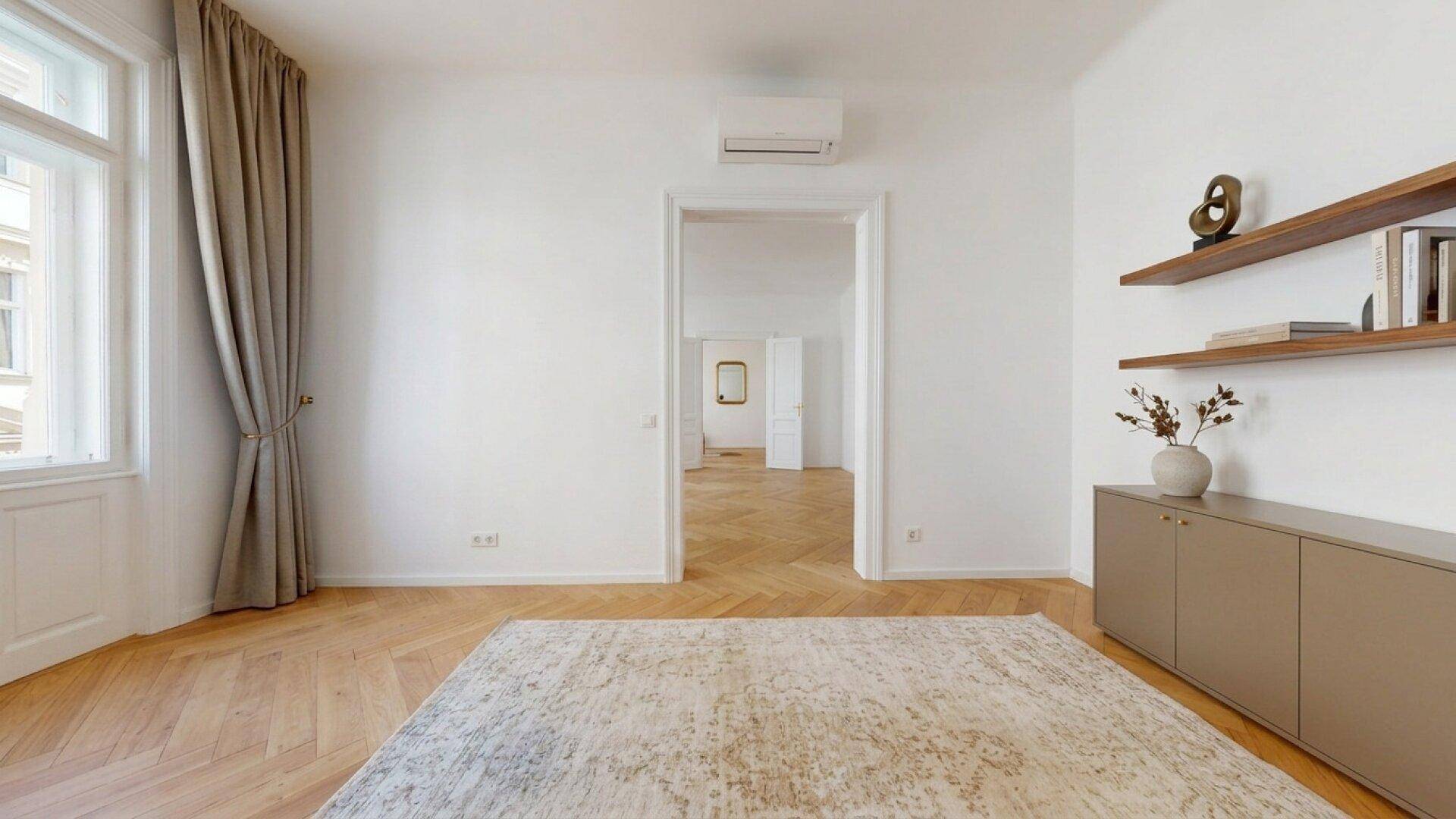 Heller Raum mit Fischgrätparkett, modernen Regalen und großem Fenster mit Vorhängen.