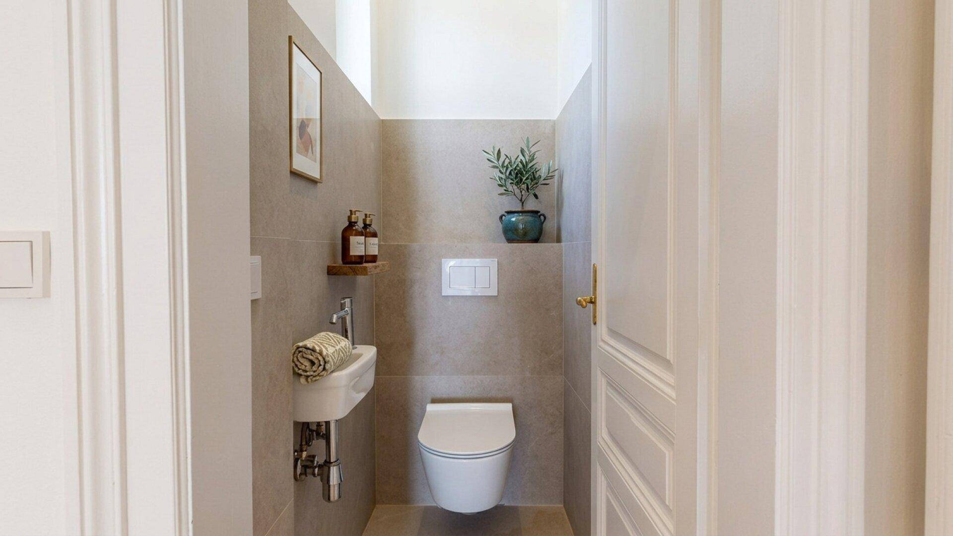 Kleines Gäste-WC mit wandhängender Toilette, kleinem Waschbecken und Fliesen.