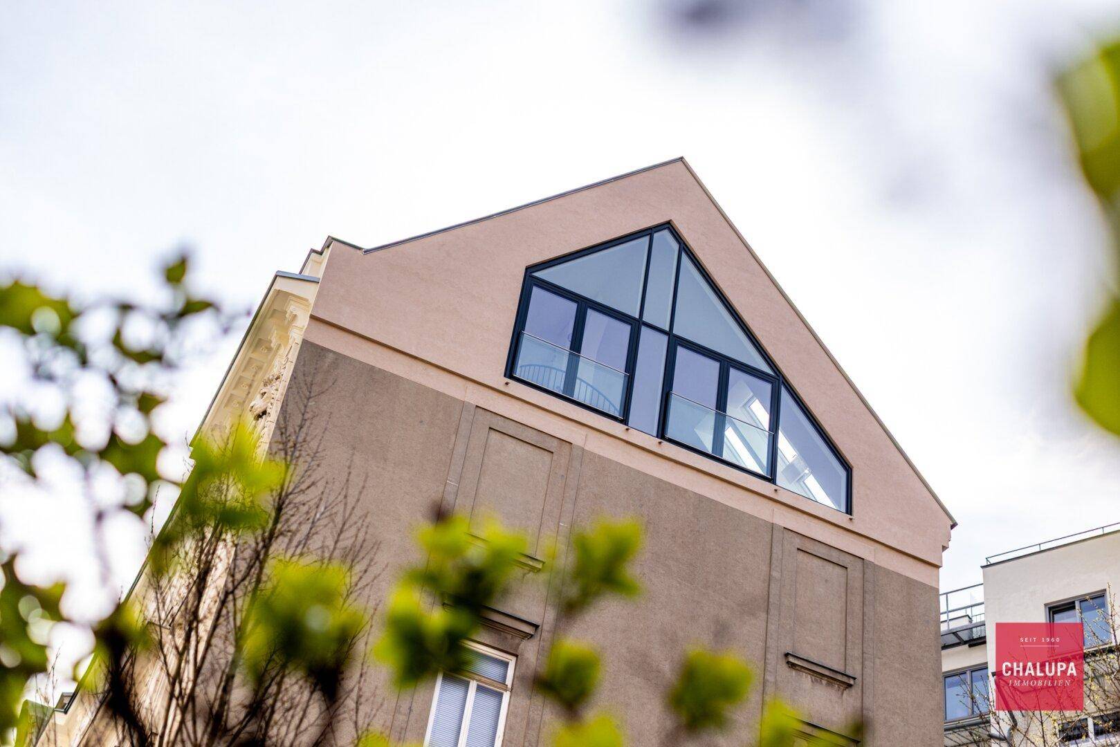 Moderne Dachgeschossfassade mit großen dreieckigen Fenstern und zeitgenössischer Architektur.