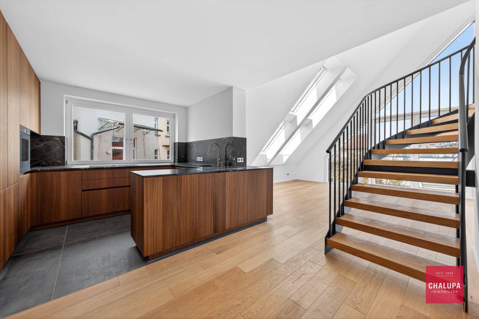 Moderne Holzküche mit dunklen Arbeitsplatten, Kücheninsel und integrierter Wendeltreppe im Dachgeschoss.