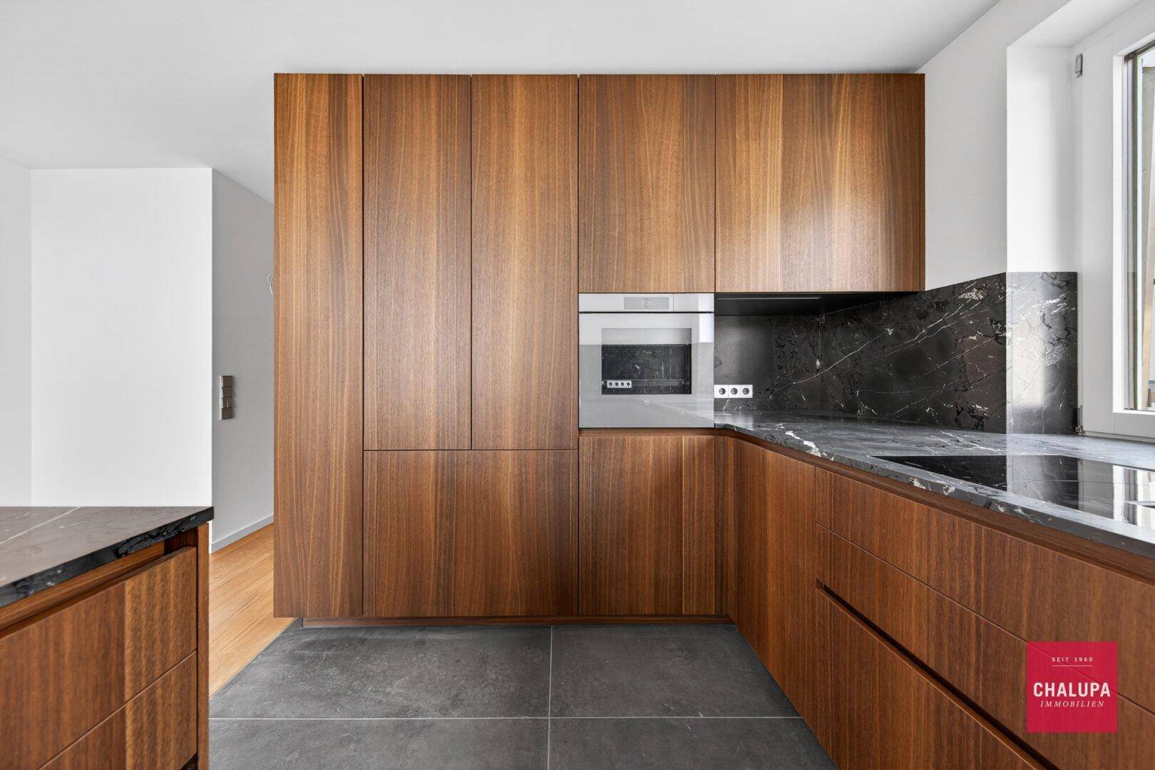 Stilvolle Holzküche mit glatten Fronten, dunklen Arbeitsplatten und integriertem Backofen.