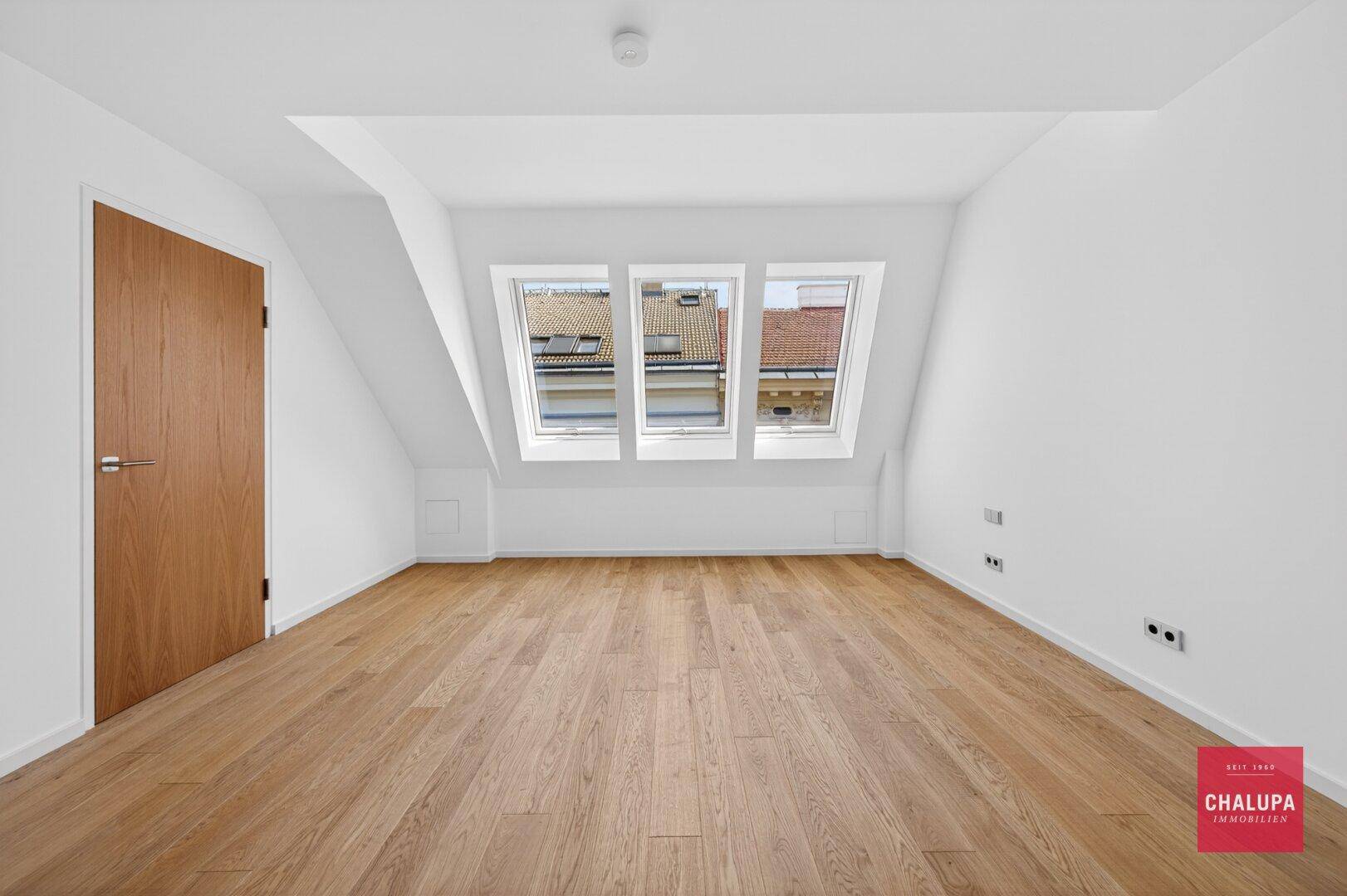 Helles Schlafzimmer mit Holzboden, Dachschrägen und drei Dachfenstern für viel Tageslicht.