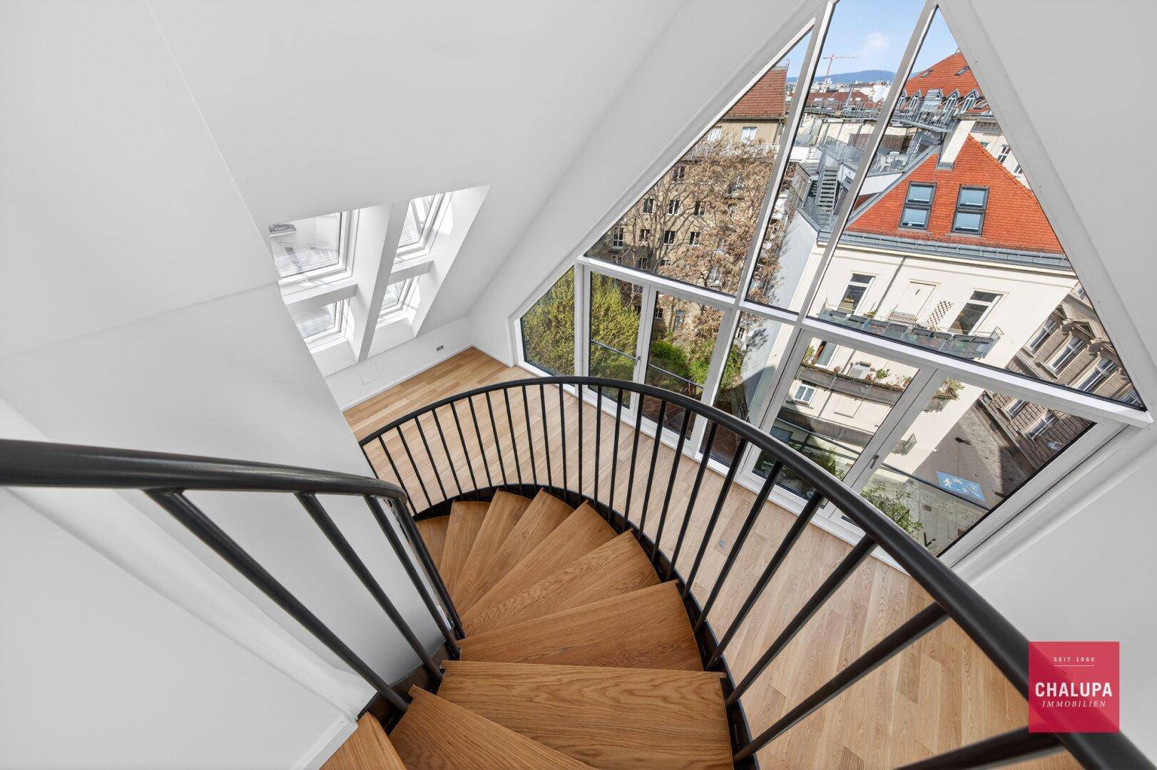 Blick von der Wendeltreppe auf die Stadt durch große, moderne Dreiecksfenster.