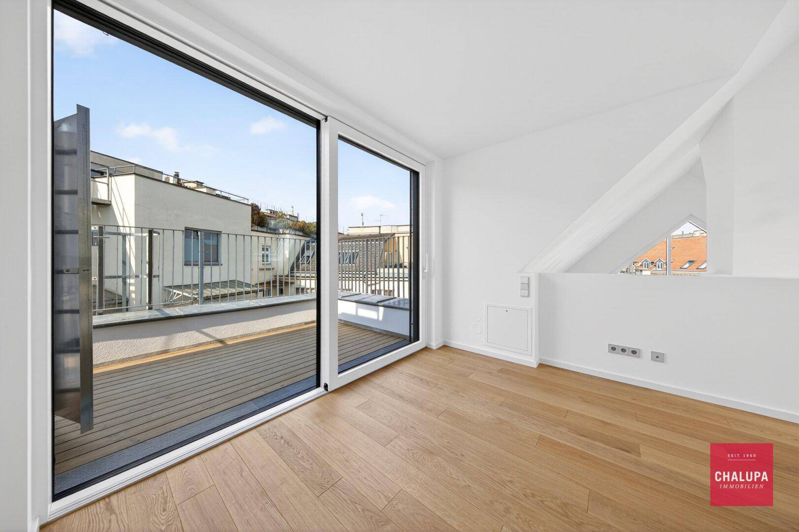 Heller Raum mit Holzboden und großen Glasschiebetüren, die zu einer Terrasse führen.