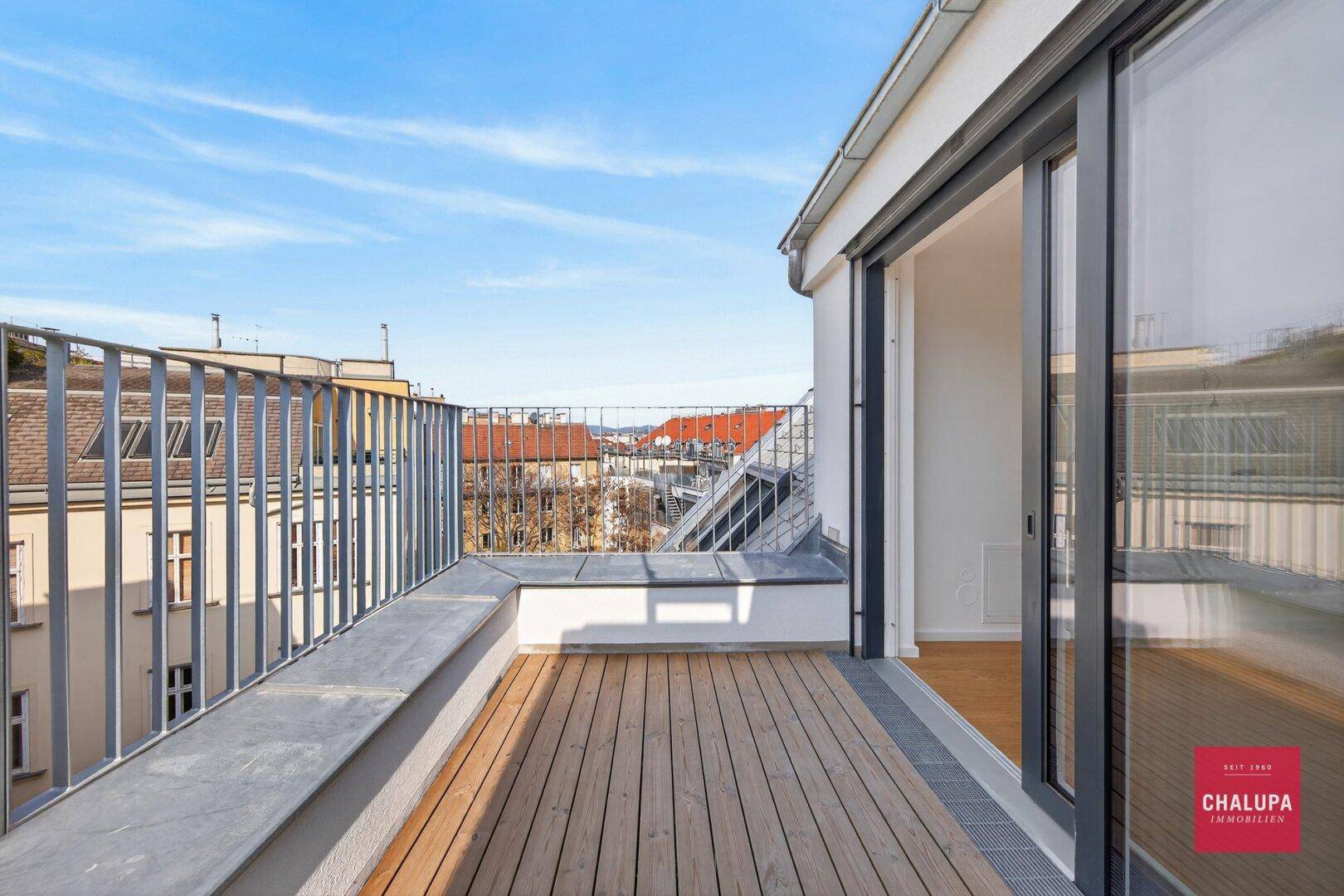 Geräumige Terrasse mit Holzboden und Metallgeländer, bietet einen weiten Blick über die Dächer der Stadt.
