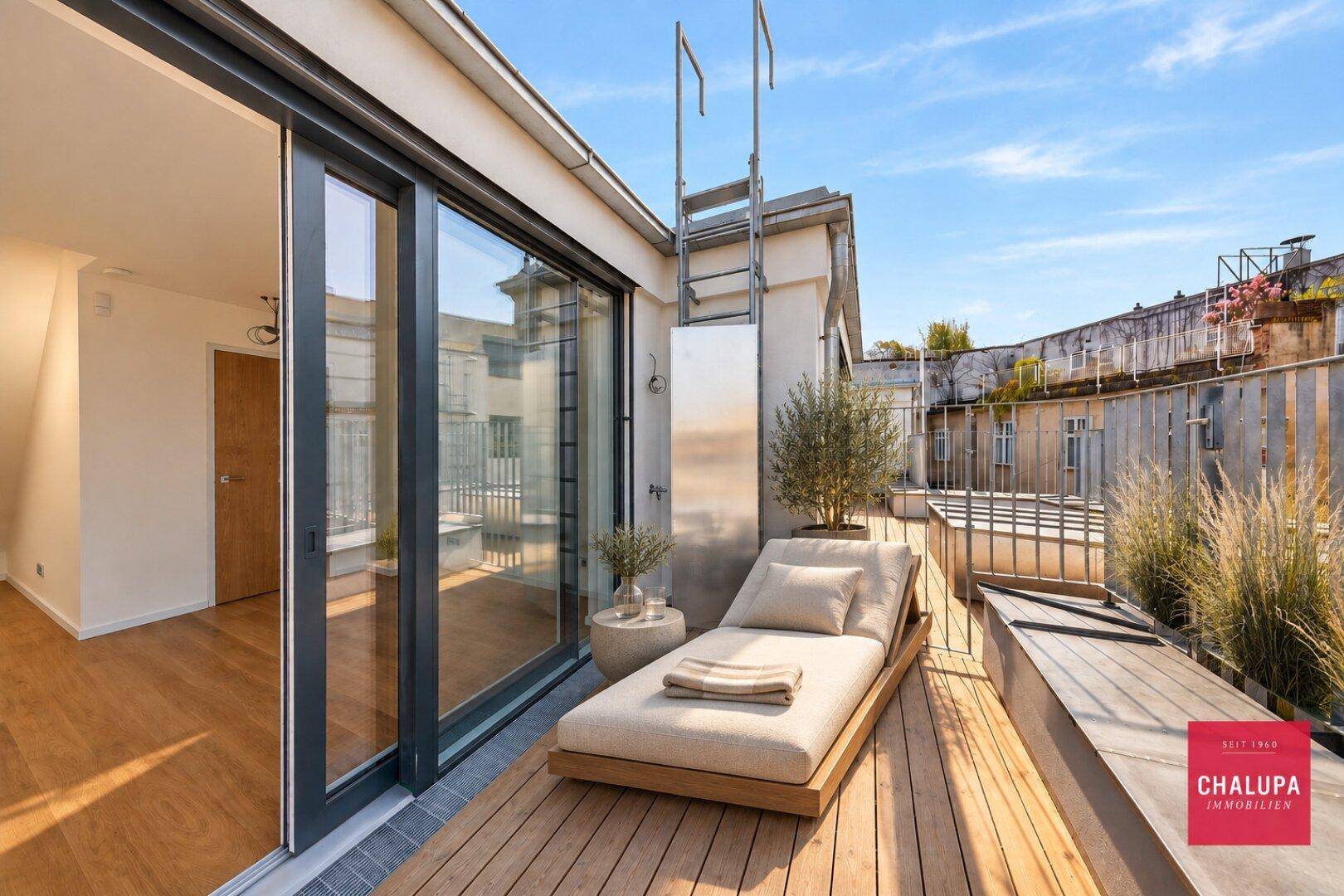 Sonnenterrasse mit Holzboden, bequemer Liege und Pflanzen, ideal zum Entspannen im Freien.