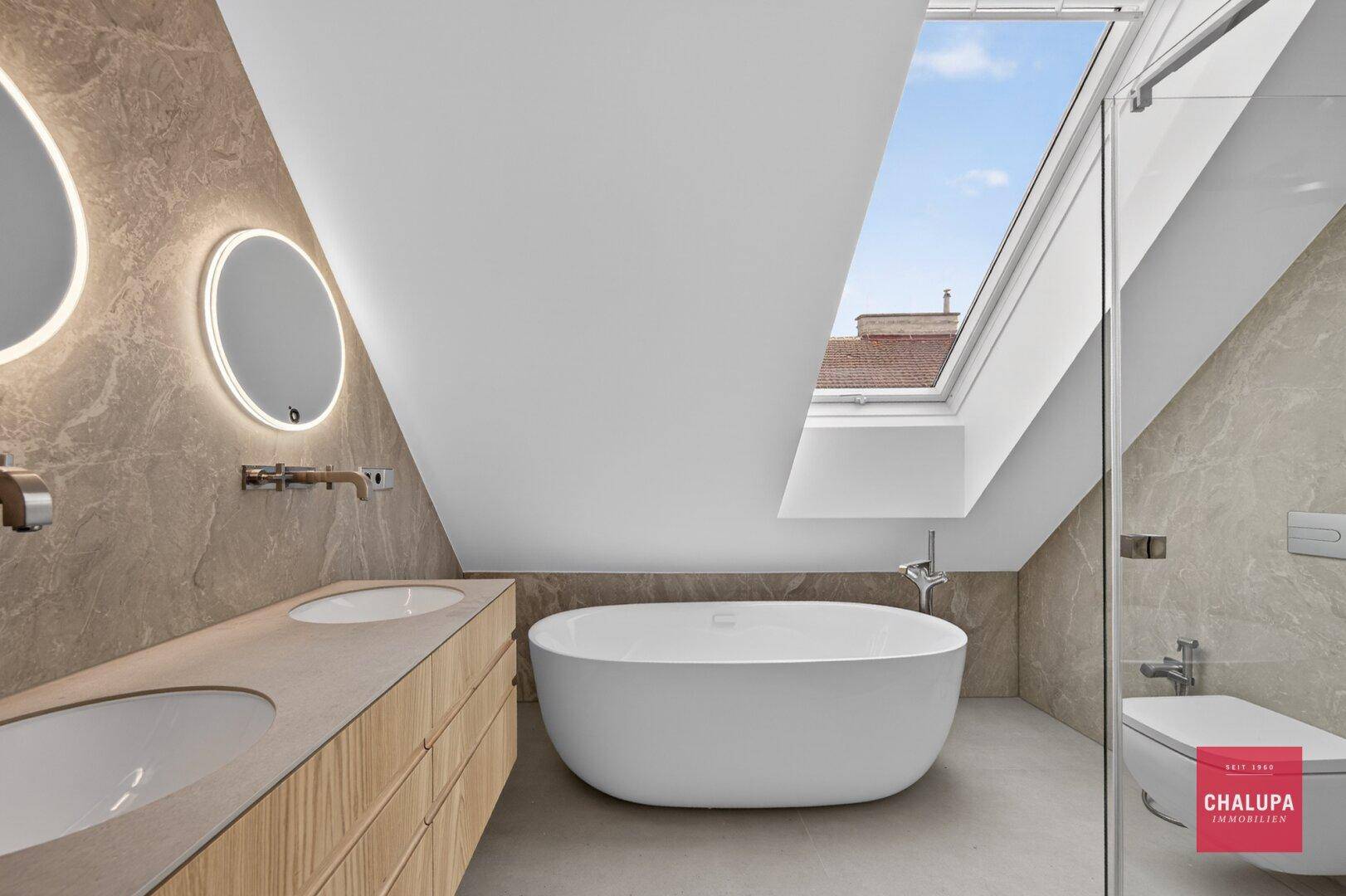 Modernes Dachgeschossbad mit freistehender Badewanne, Doppelwaschbecken und großem Dachfenster.