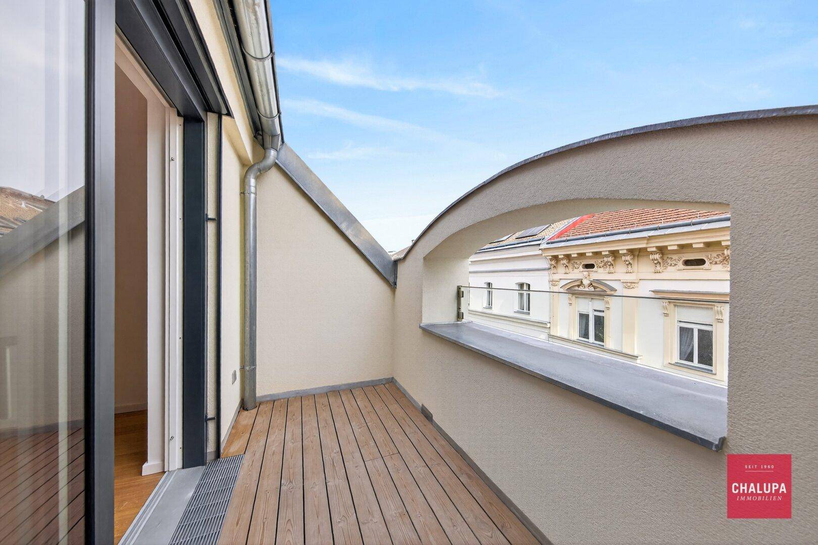 Attraktiver Balkon mit Holzdeck und Blick auf die umliegenden Gebäude.