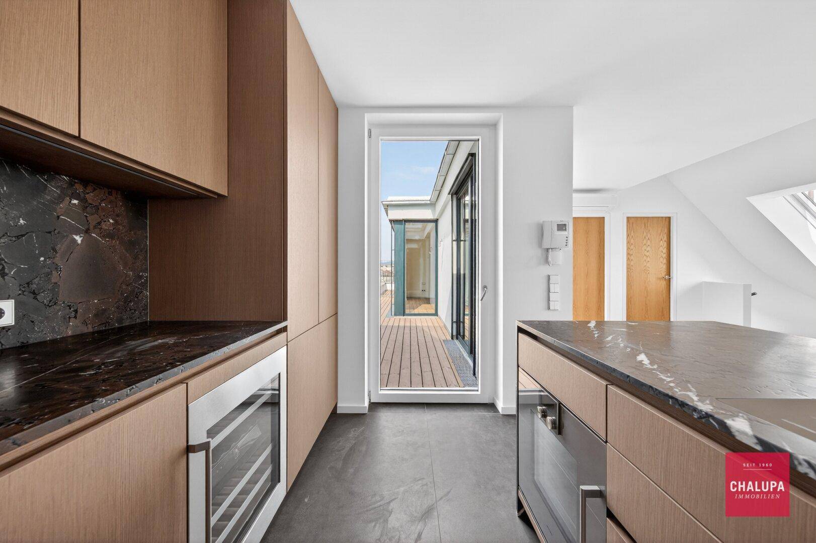 Helle Küche mit Holzfronten, dunkler Arbeitsplatte und direktem Zugang zur Terrasse.