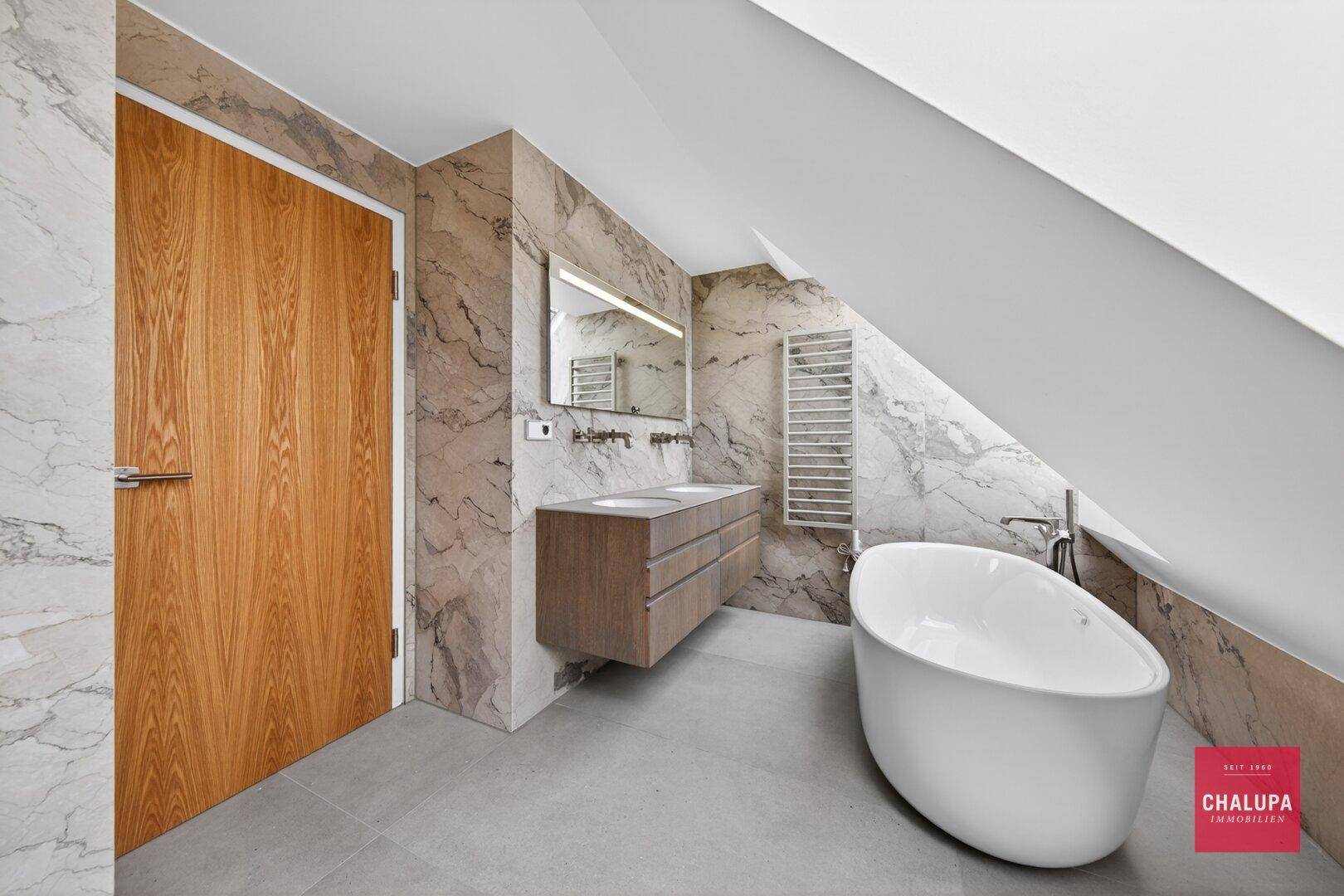 Modernes Dachgeschossbad mit freistehender Badewanne, Doppelwaschbecken und beheiztem Handtuchhalter.