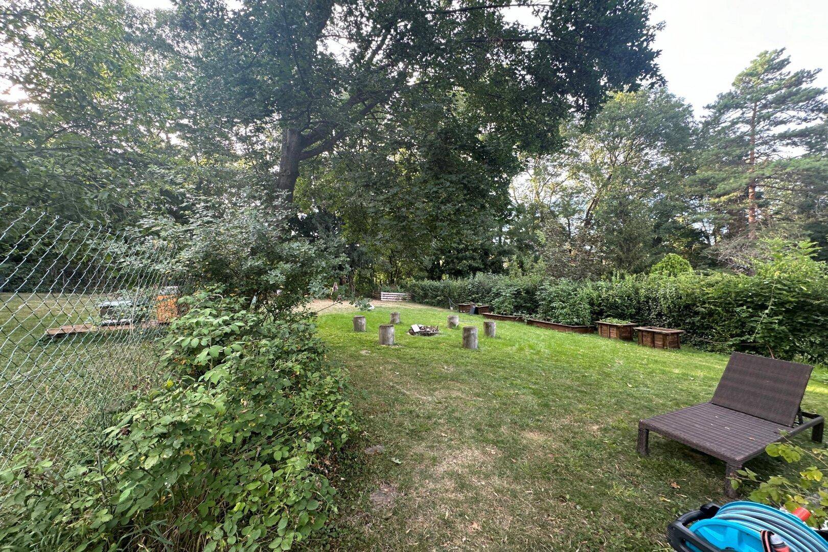 Großer Gartenbereich mit Rasenfläche, Bäumen und einer Feuerstelle für gesellige Abende.