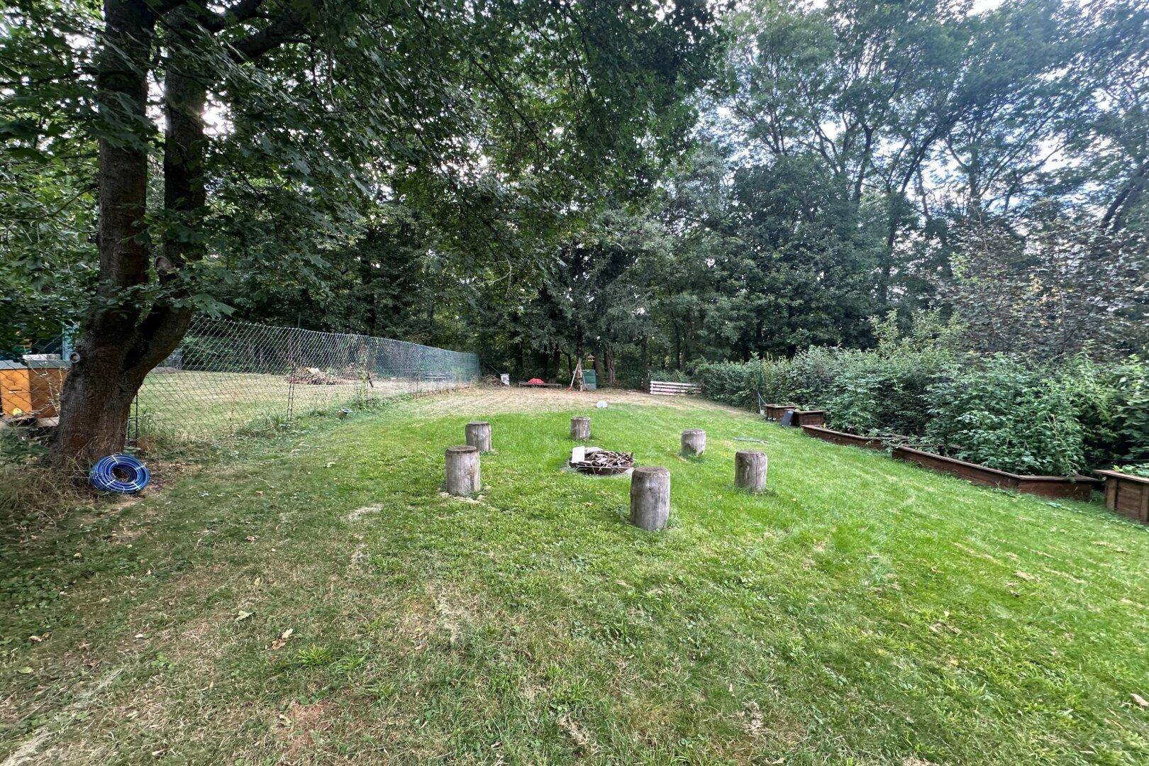 Weitläufiger Garten mit Rasen, alten Bäumen und einer vorbereiteten Feuerstelle.