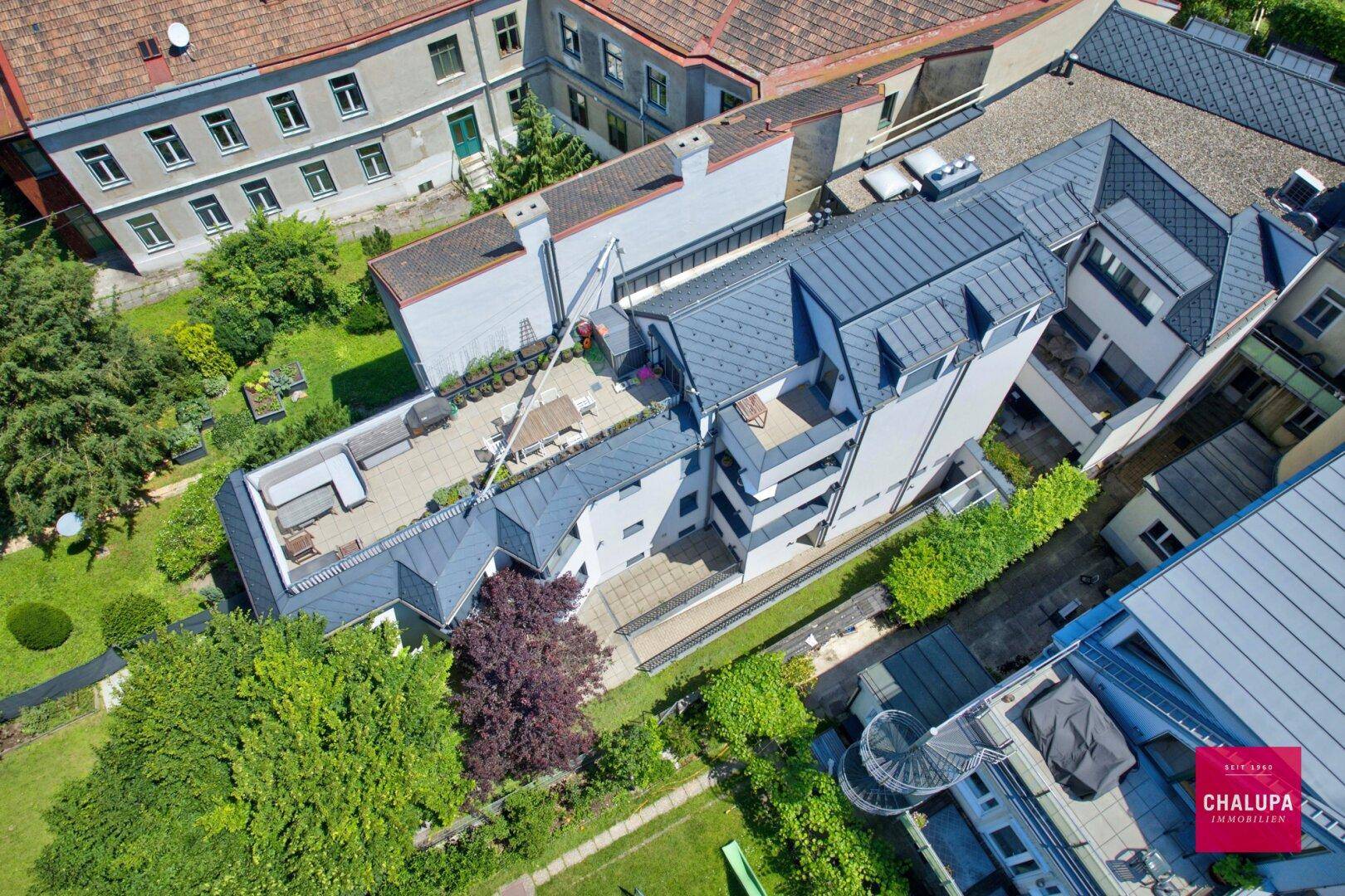 Luftaufnahme eines modernen Wohnkomplexes mit mehreren Terrassen, Gärten und umliegenden Gebäuden.