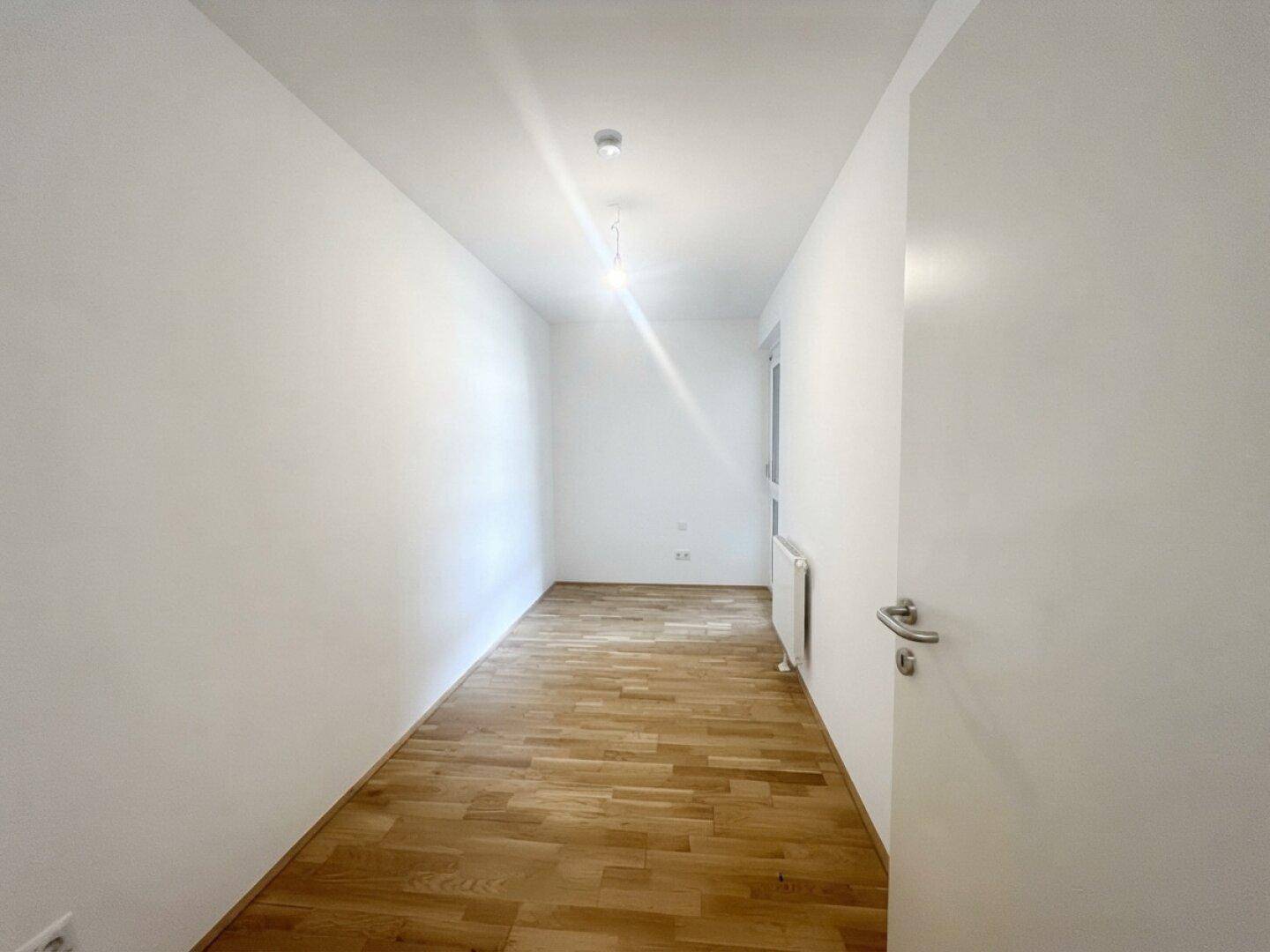 Leeres Schlafzimmer mit Parkettboden, weiß gestrichenen Wänden und einem Fenster.