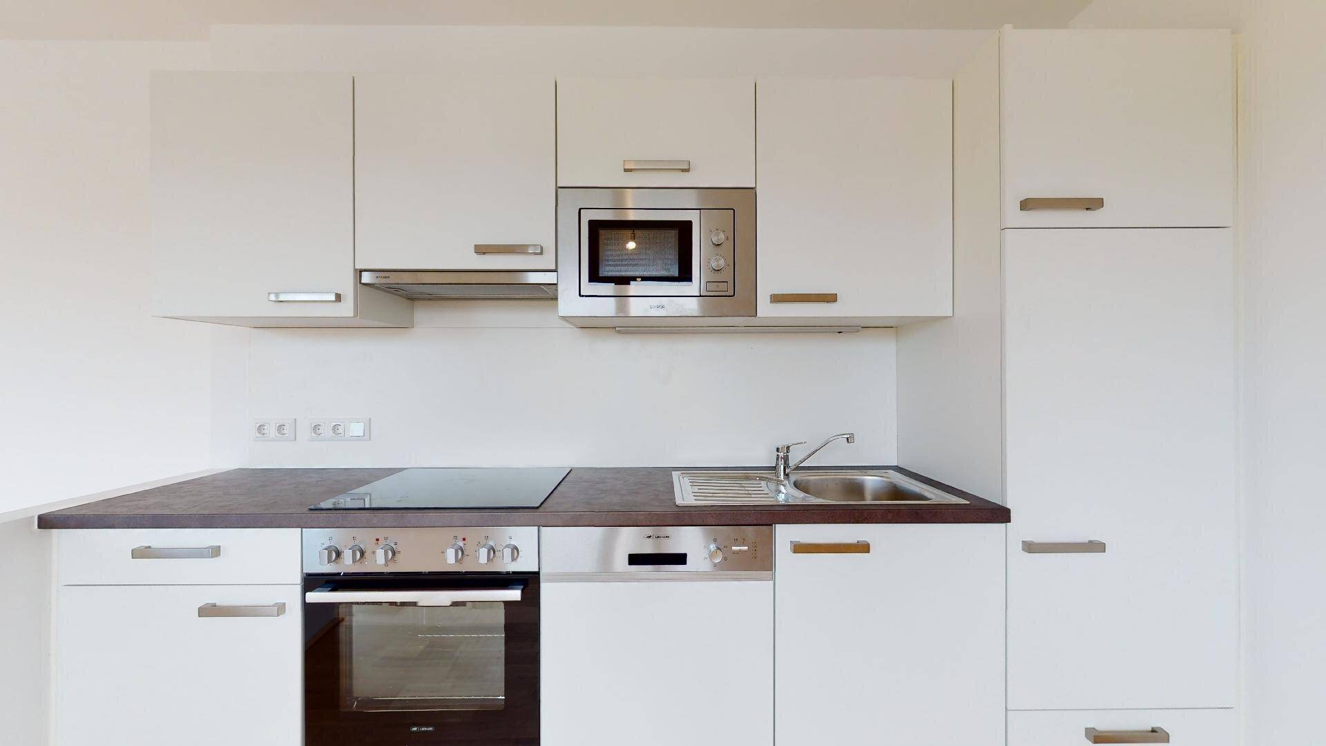 Moderne Einbauküche mit weißen Schränken, integrierten Geräten und dunkler Arbeitsplatte.