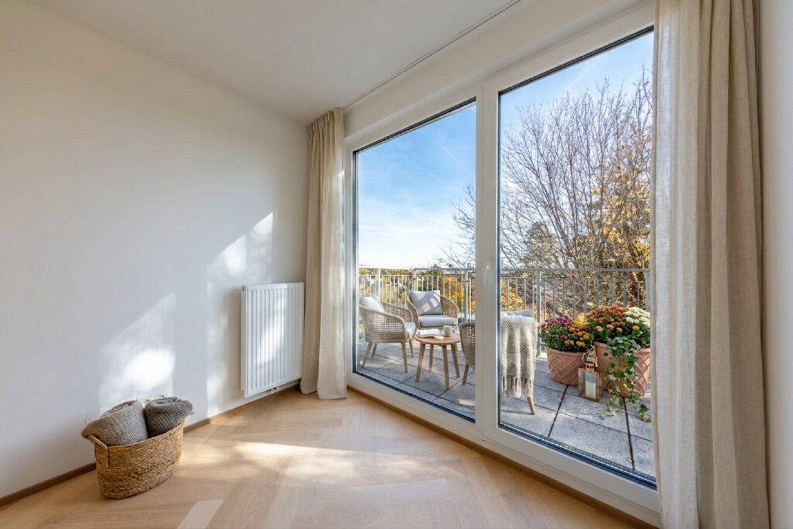 Helles Zimmer mit großen Fenstern und Zugang zu einem möblierten Balkon.