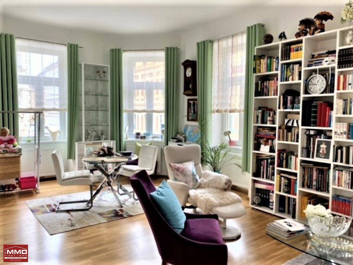 Geräumiges Wohnzimmer mit mehreren Fenstern, Bücherregal und gemütlicher Sitzecke.