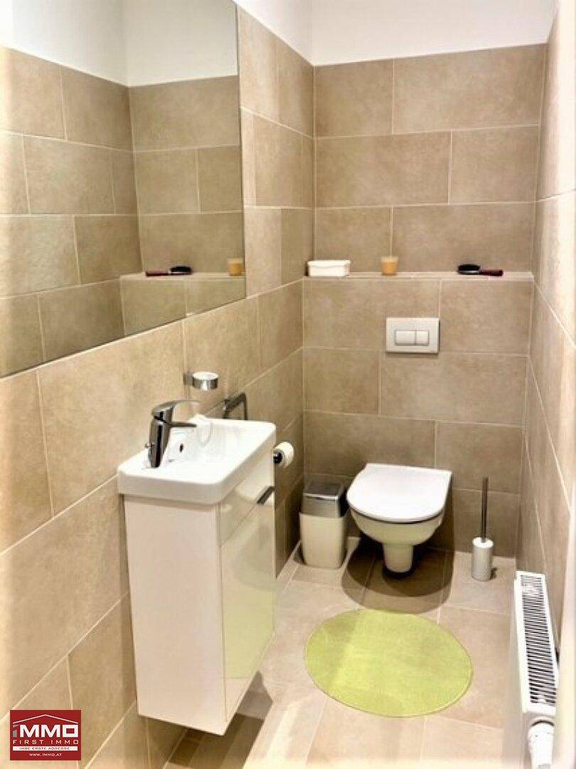 Modernes Gäste-WC mit beigefarbenen Fliesen, wandhängendem WC und kleinem Waschbecken.