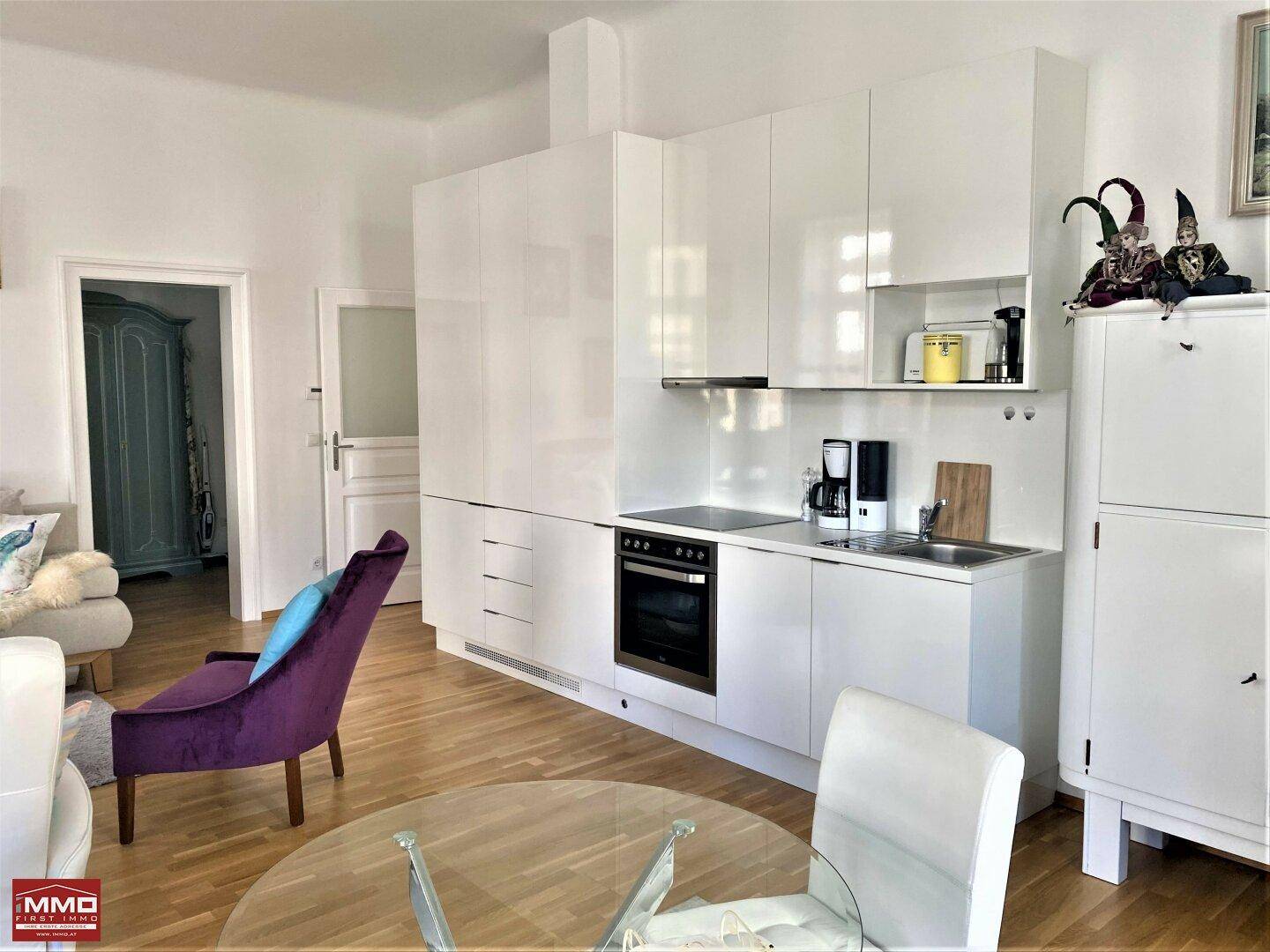 Moderne Küchenzeile mit weißen Hochglanzschränken, integriertem Backofen und Kochfeld.