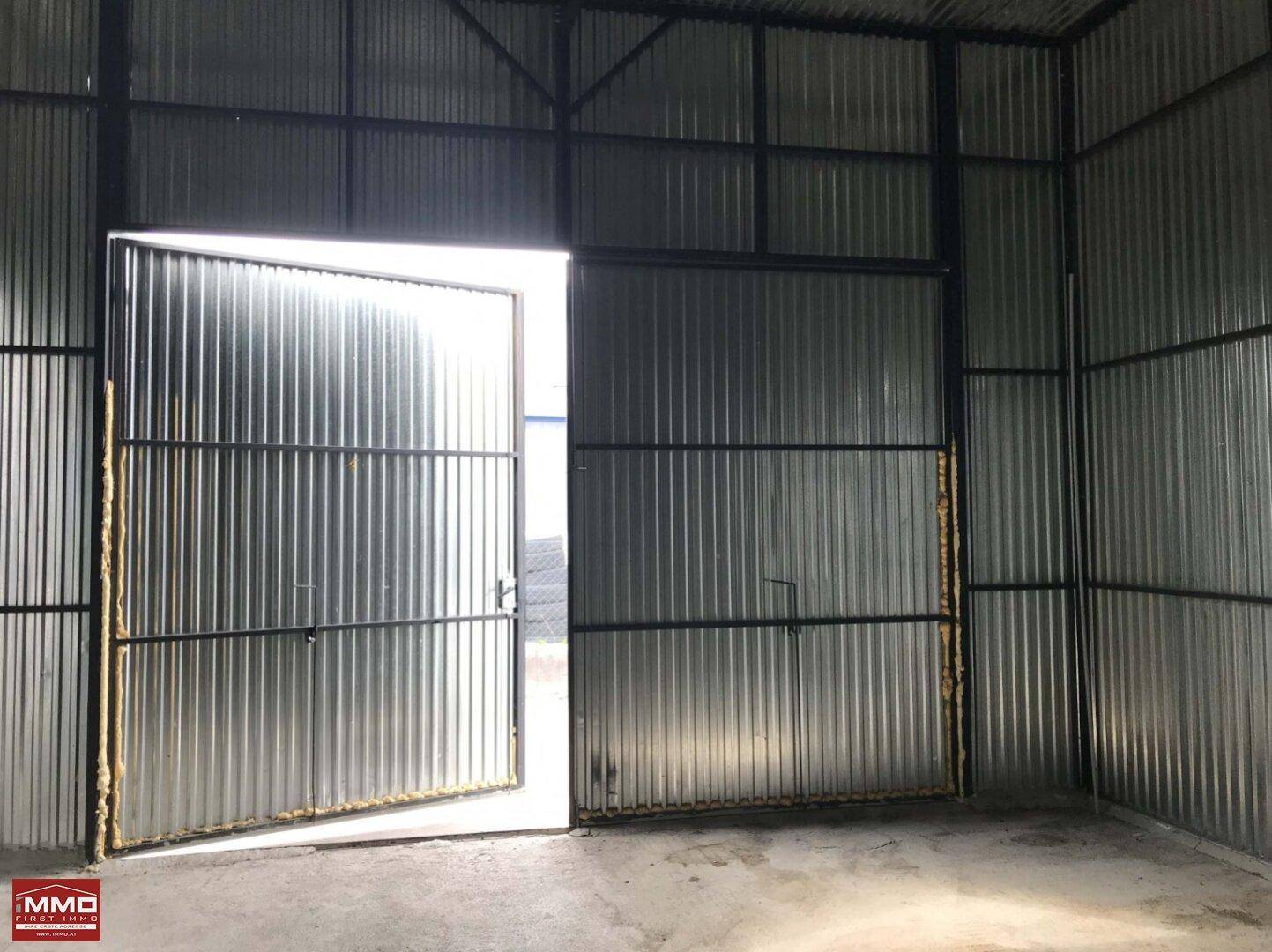 Blick in die Lagerhalle mit geöffnetem Wellblechtor, das Tageslicht hereinlässt.