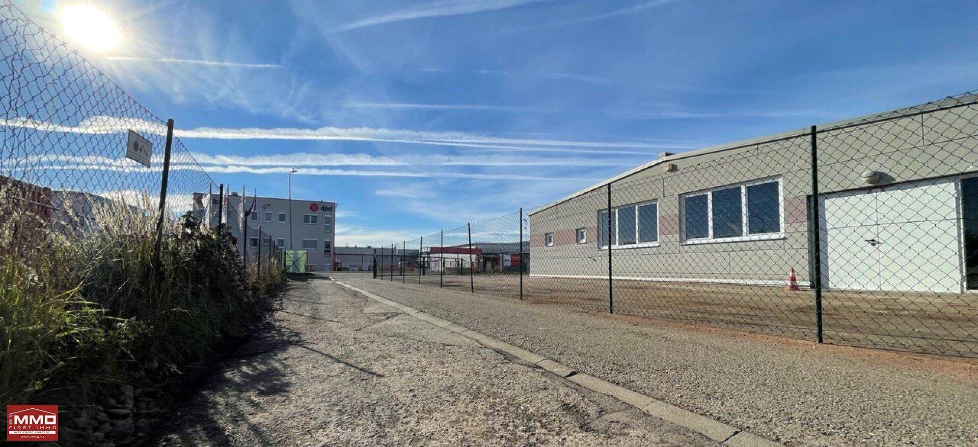 Außenansicht eines Industriegebäudes mit Zaun im Vordergrund unter weitem blauem Himmel.