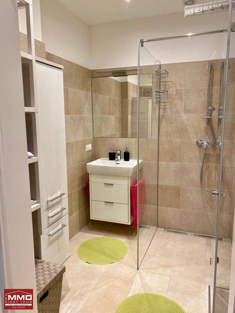 Modernes Badezimmer mit beigefarbenen Fliesen, ebenerdiger Dusche und elegantem Waschbecken.