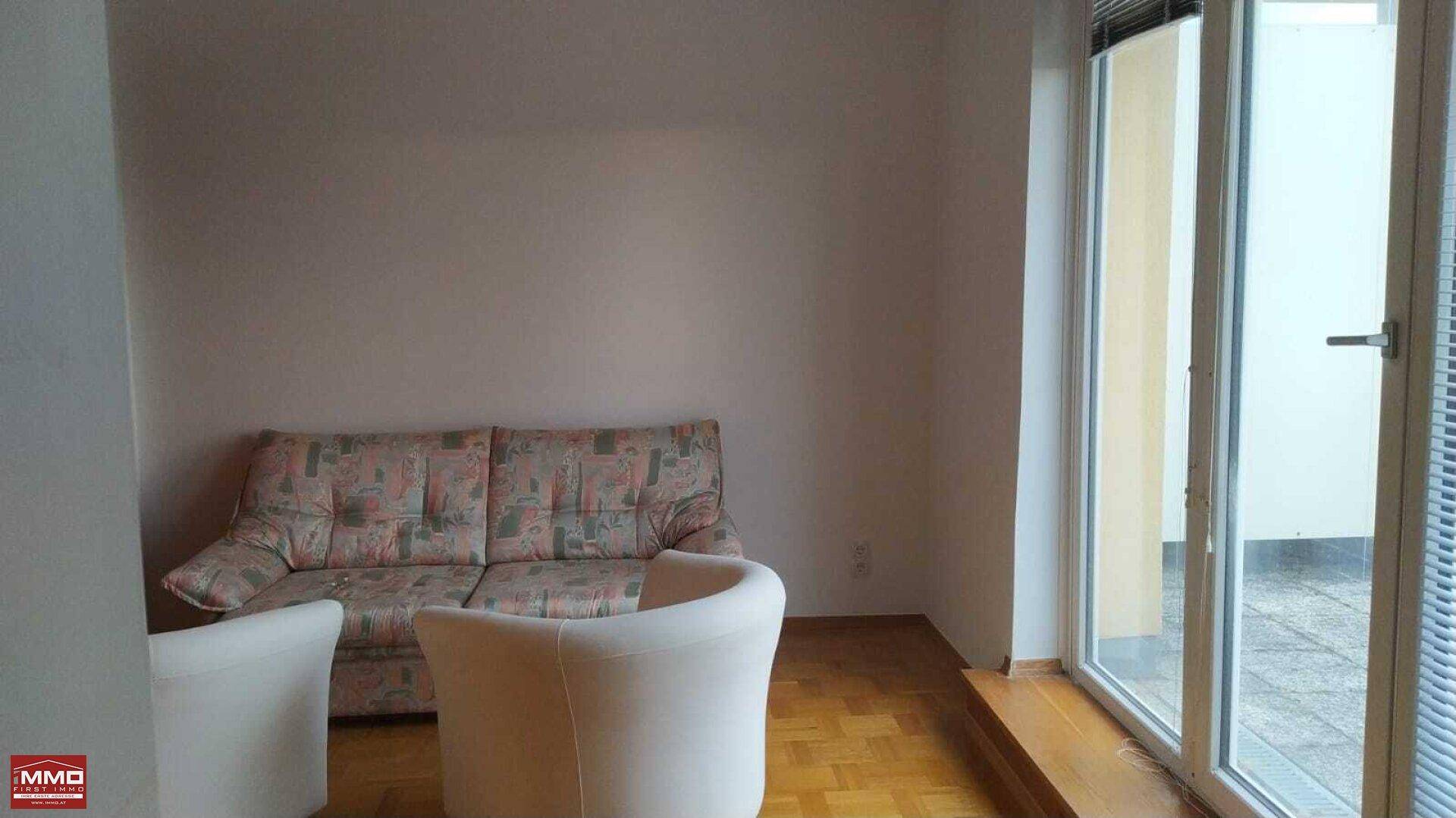 Helles Wohnzimmer mit Parkettboden, Sofa und Zugang zu einer Außenterrasse.
