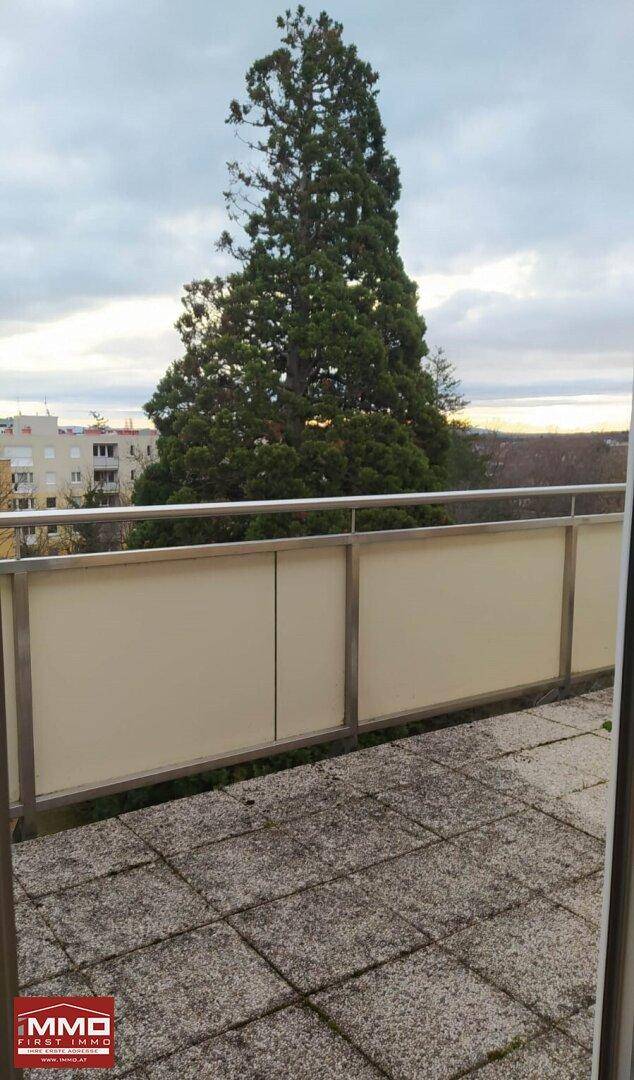 Geräumige Terrasse mit Fliesenboden und Blick auf Bäume und die Umgebung.