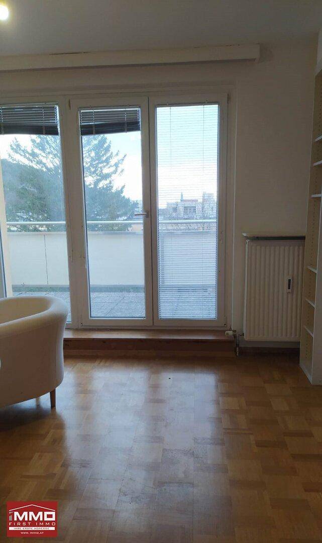 Wohnbereich mit Parkettboden, Heizkörper und großen Fenstern mit Stadtblick.