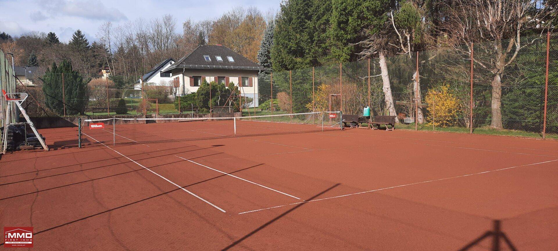 Weitläufiger Tennisplatz mit rotem Sand und umliegender grüner Landschaft, ideal für Sportbegeisterte.