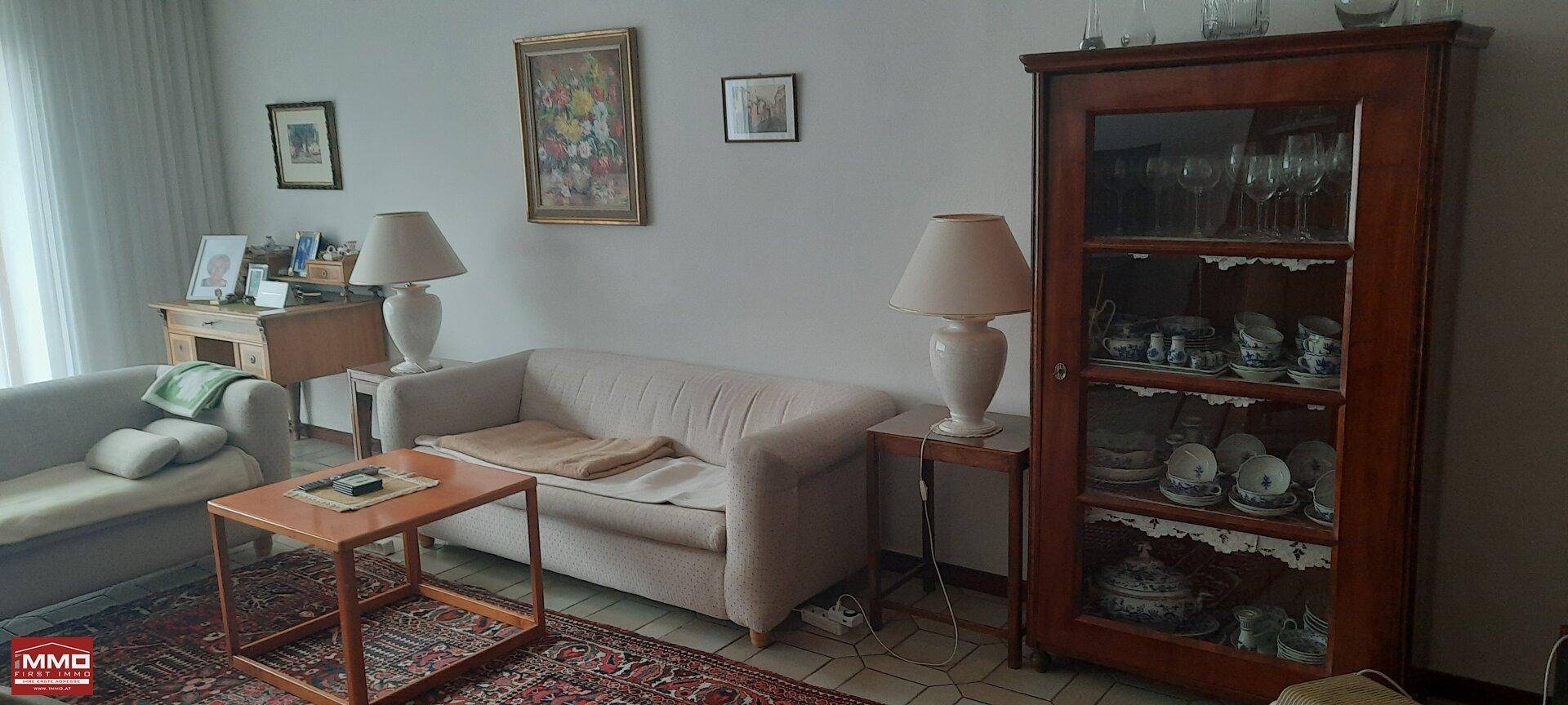 Wohnzimmer mit zwei Sofas, Beistelltischen und einem antiken Vitrinenschrank.