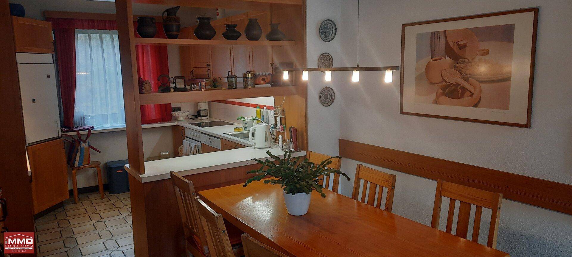 Essbereich mit Holztisch und Blick in die angrenzende Küche, beleuchtet von einer modernen Hängelampe.
