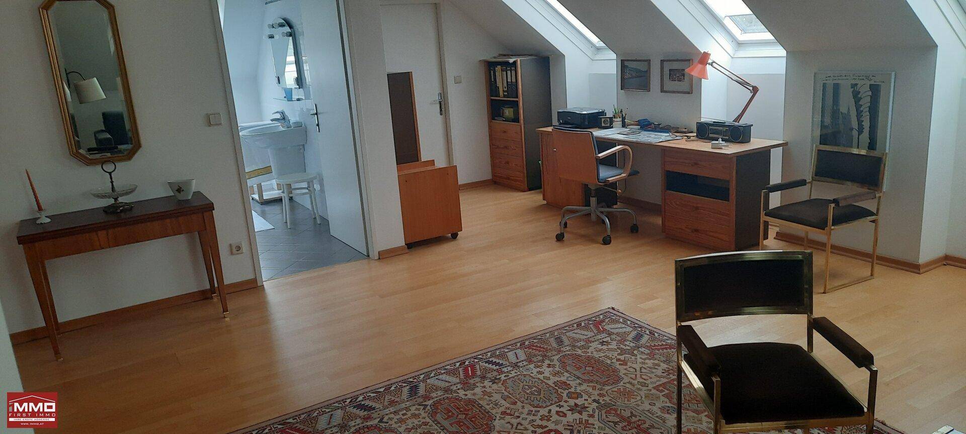 Dachgeschosszimmer mit Holzboden, Schreibtisch und Zugang zu einem Badezimmer.