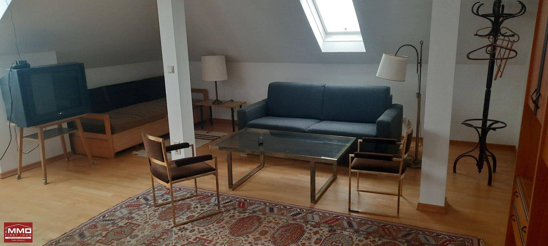 Gemütliches Wohnzimmer im Dachgeschoss mit Sofa, Teppich und Dachfenster für natürliches Licht.