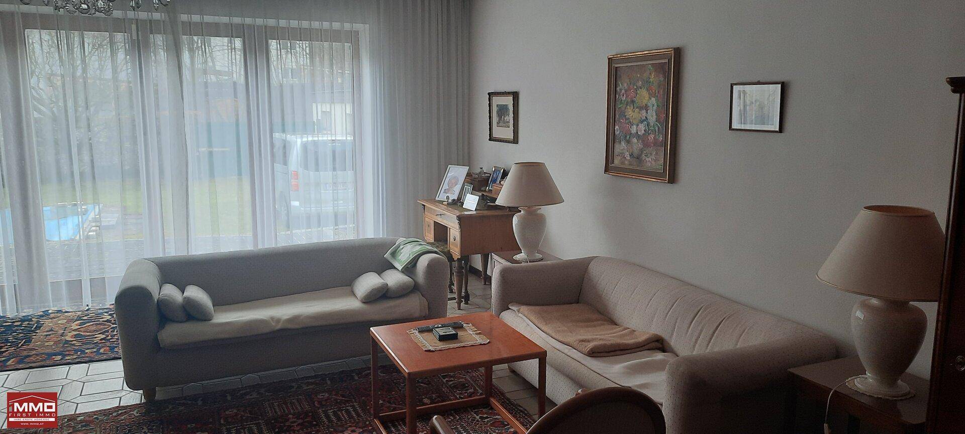 Helles Wohnzimmer mit bequemen Sofas und großen Fenstern mit Blick ins Grüne.