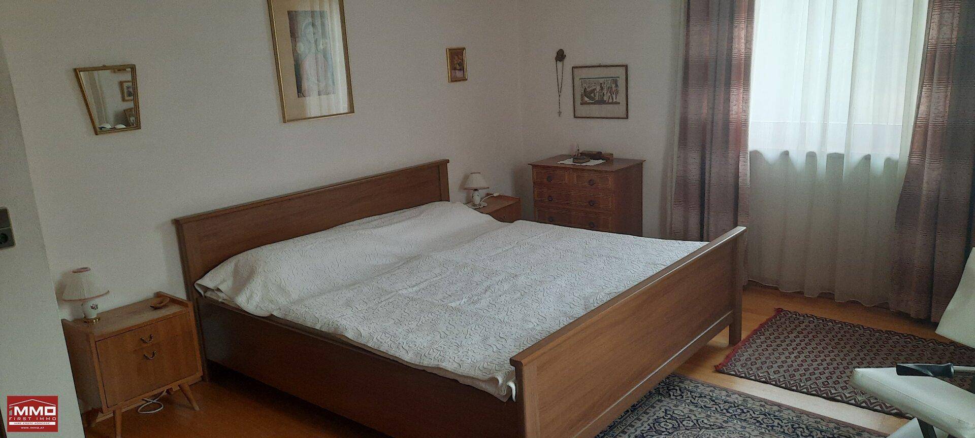 Schlafzimmer mit Doppelbett, Holzmöbeln und einem Fenster mit Vorhängen.