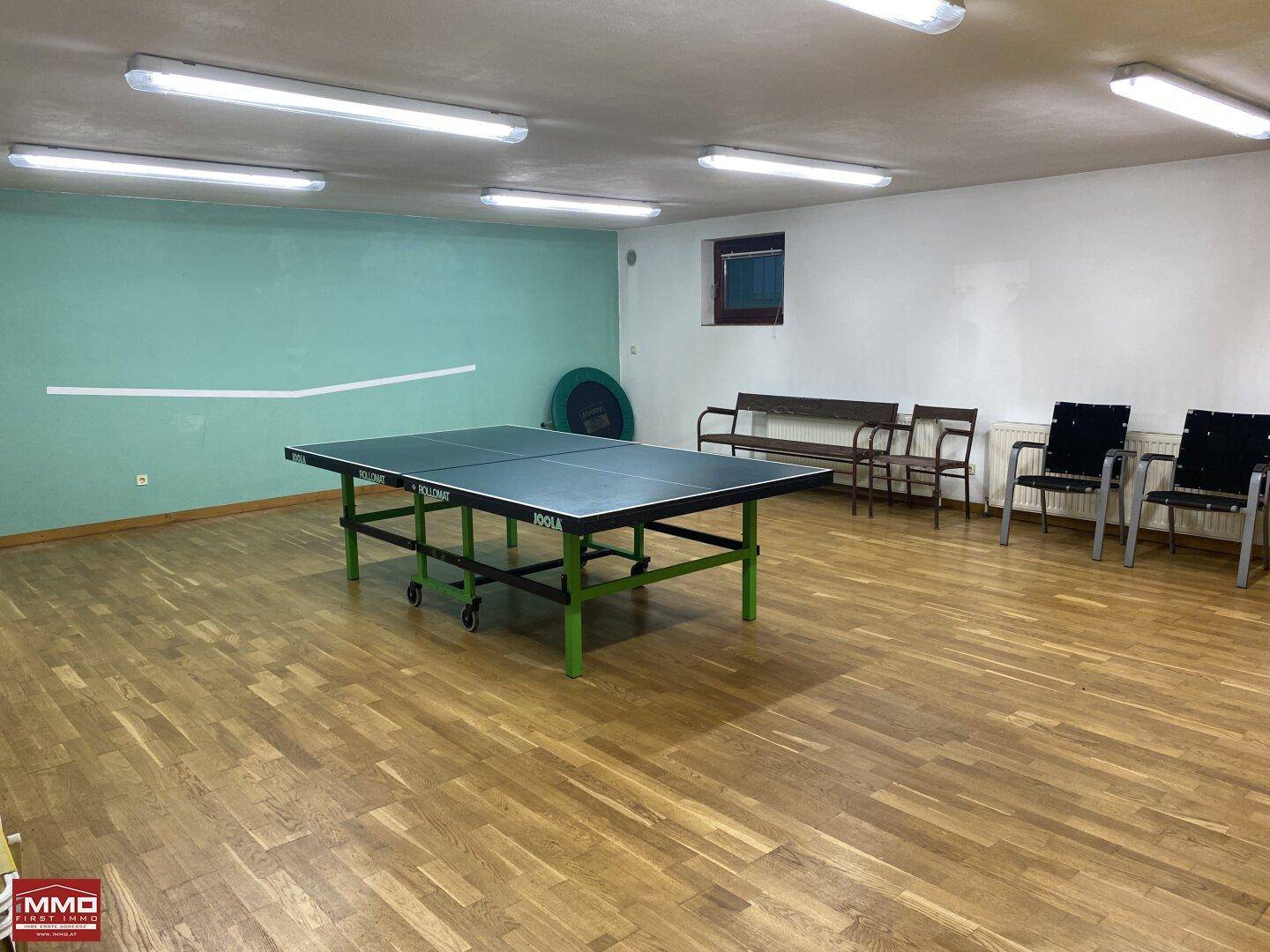 Großer Raum mit Tischtennisplatte und Sitzgelegenheiten, ideal für Sport und Freizeit.